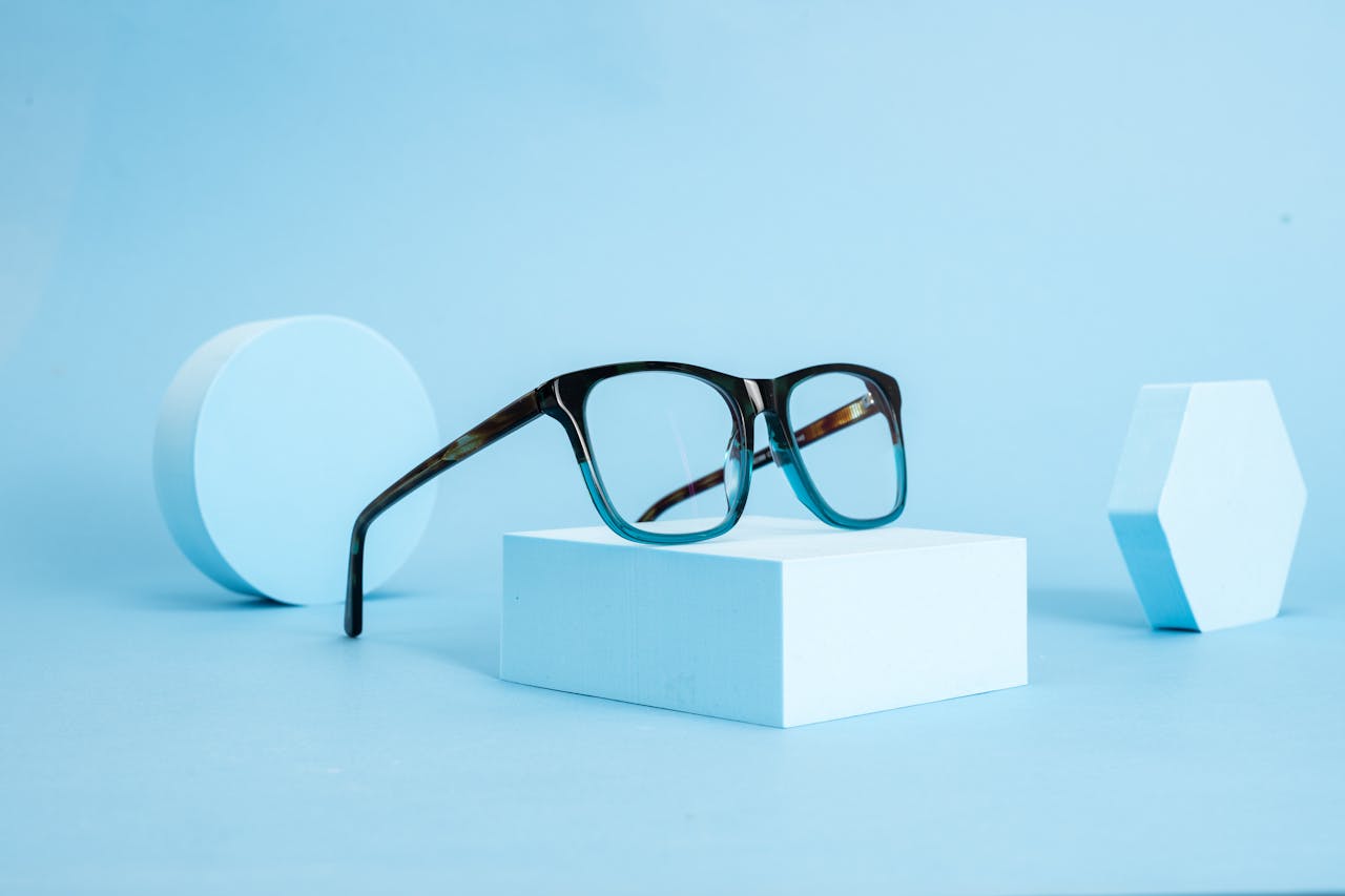 Stylish eyeglasses displayed on geometric shapes with a blue minimalist theme.
