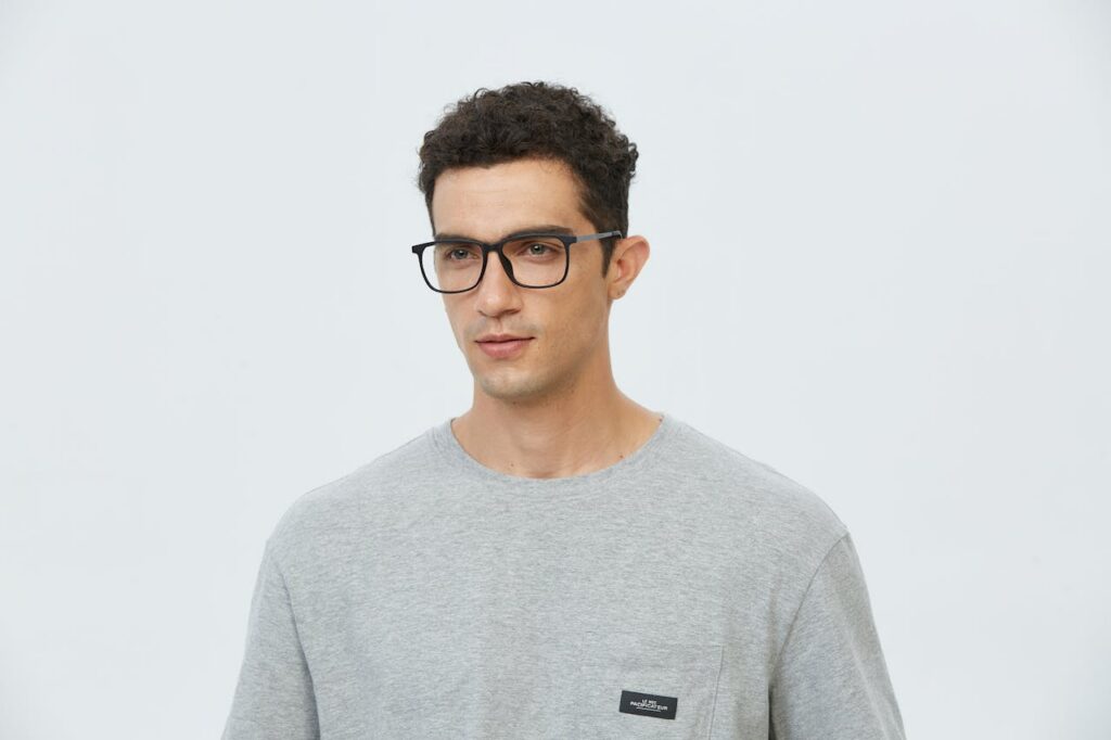 pexels-photo-27603695 Portrait of a young man wearing glasses in a casual gray t-shirt, looking pensive.