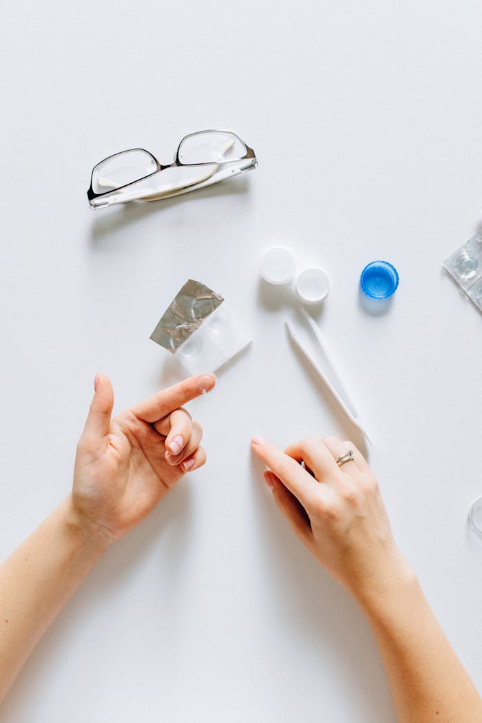 Flatlay of contact lens supplies with glasses and hands, ideal for vision care themes.