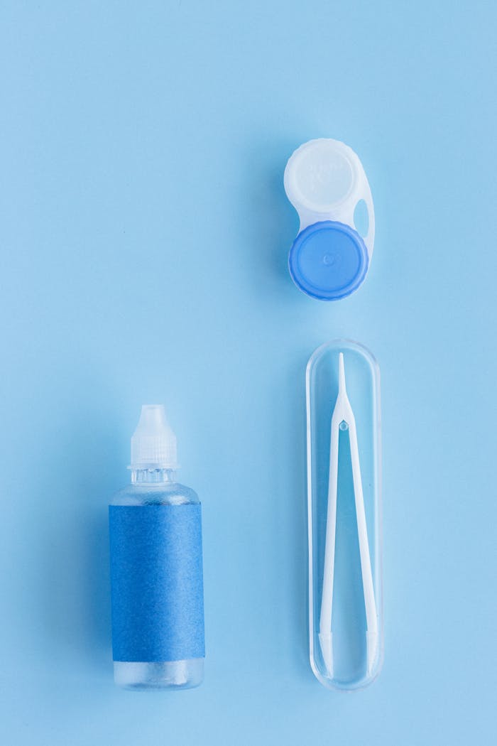 Flat lay of contact lens case, solution bottle, and tweezers on a blue background.